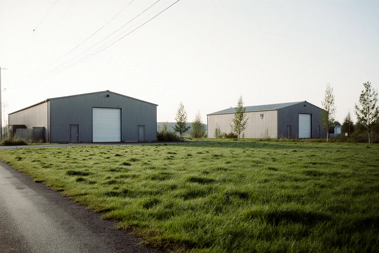 Open grassy land beside a road with low industrial buildings in the background